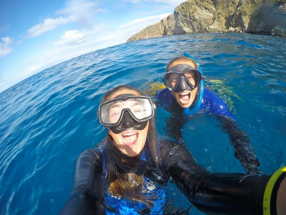 Two staff members in scuba diving gear taking a selfie in the water.