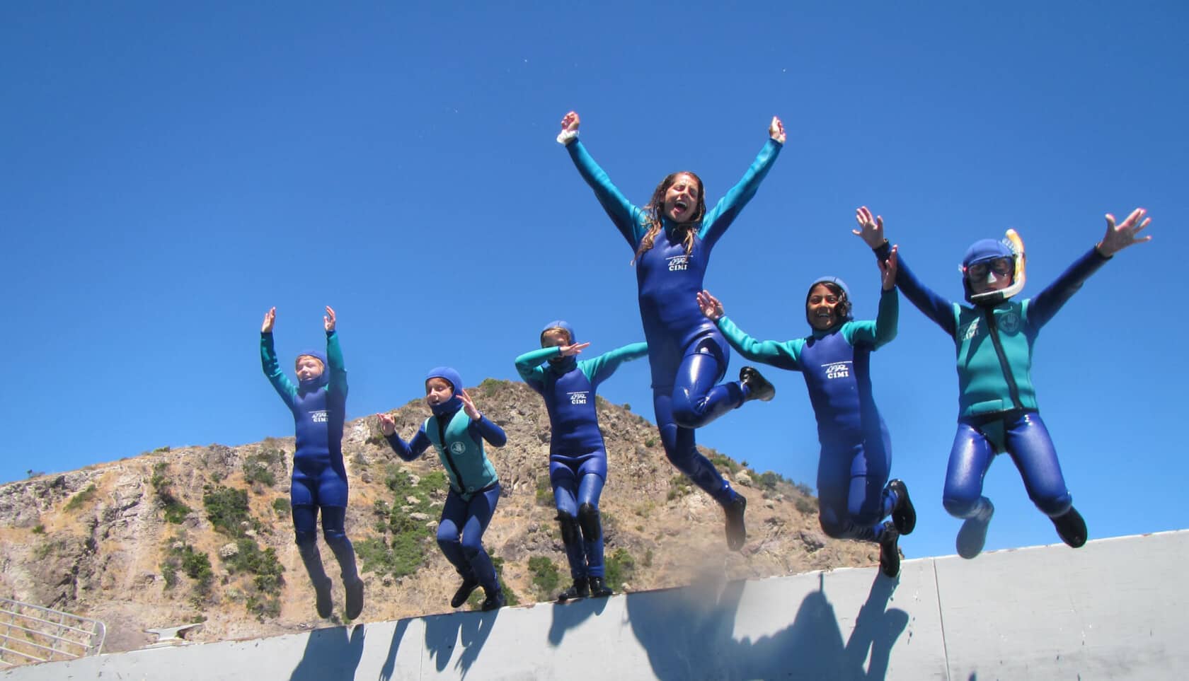 A group of campers in wetsuits, jumping into the water.