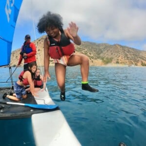A camper jumping into the water from a sailboat.