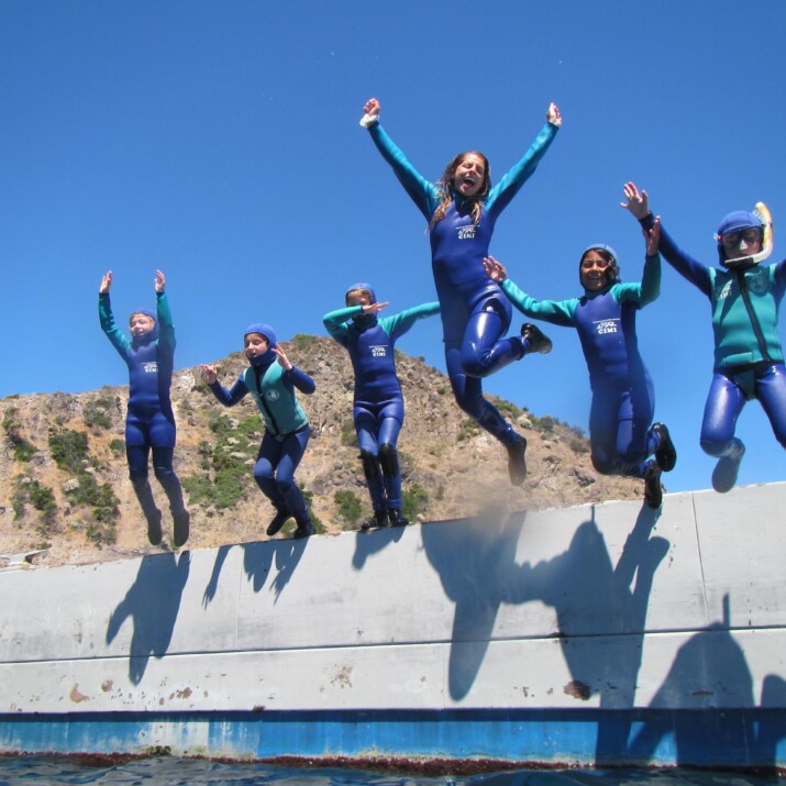 A group of campers in wetsuits, jumping into the water.