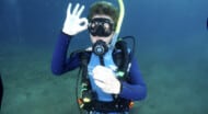 A camper open water scuba diving, signaling that they are okay.