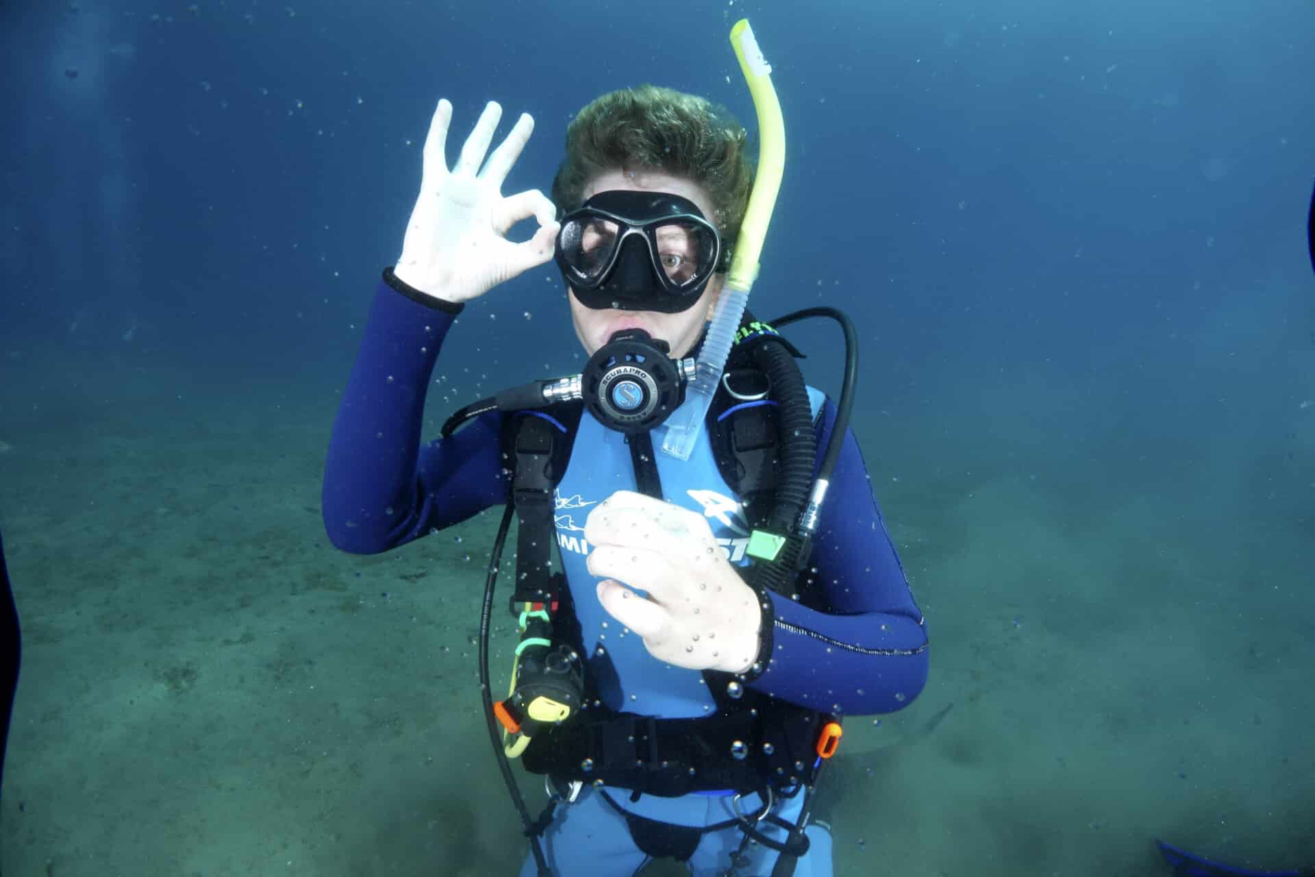 A camper open water scuba diving, signaling that they are okay.
